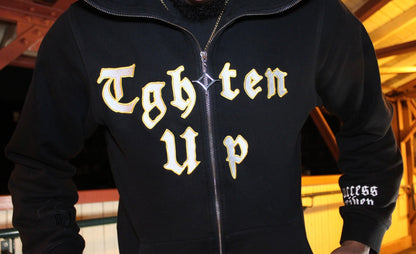 Black hoodie with gold text 'Tghten Up' worn by a person